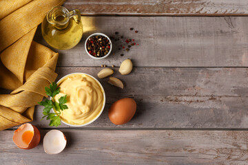 Bowl with tasty mayonnaise sauce and ingredients on grey wooden background