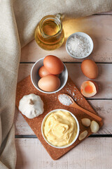 Bowl with tasty mayonnaise sauce and ingredients on light wooden background