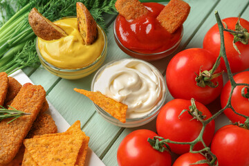 Bowls of different sauces with dipped snacks and tomatoes on green wooden table