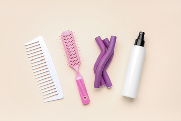 Hair brushes with curlers and spray bottle on beige background