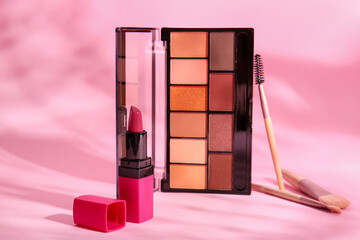 Decorative cosmetics with makeup brushes on pink background