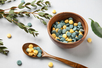 Bowl with pills, spoon and plant branches on white background, closeup