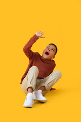 Scared little African-American boy on yellow background
