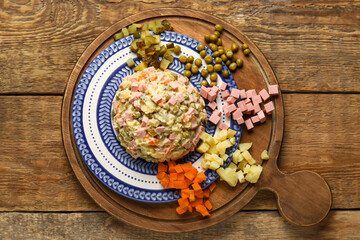 Plate of tasty Olivier salad and ingredients on wooden background