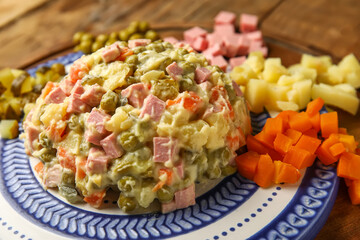 Plate of tasty Olivier salad and ingredients on table, closeup