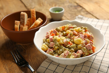 Bowl of tasty Olivier salad on wooden background