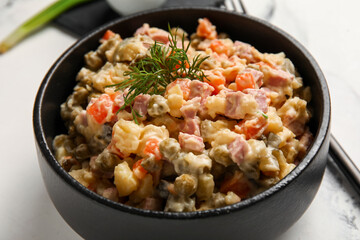 Bowl of tasty Olivier salad on white marble background, closeup