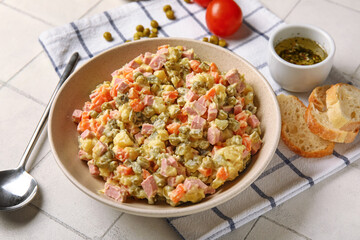 Bowl of tasty Olivier salad on white tile background
