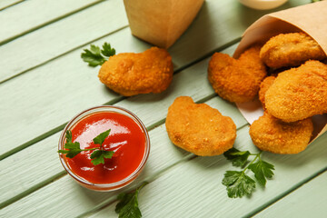 Bowl of tasty ketchup and nuggets on green wooden background
