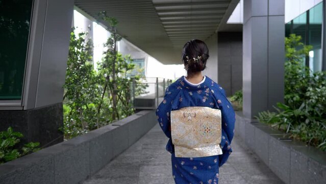 Asian woman in a traditional Japanese kimono walking in business district in central Tokyo, view from the back of a Japanese woman in a kimono walking in front of a skyscraper. 