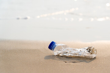 Fototapeta na wymiar empty drinking water bottle garbage plastic pollution on the sand sea beach, plastic wastes physical and chemical properties environmental ocean problems impact ecosystem and marine life