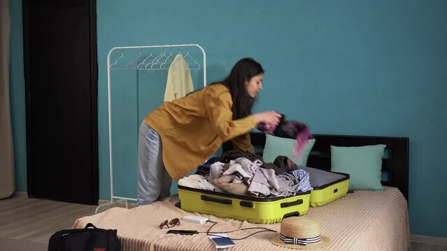 Hispanic woman putting clothes in open suitcase lying on bed. Preparation travel suitcase at home. Travel concept.