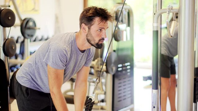 man lifting weights doing cable pushdown exercises in gym