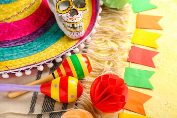 Mexican maracas with sombrero hat, painted skull, serape and flags on yellow background, closeup