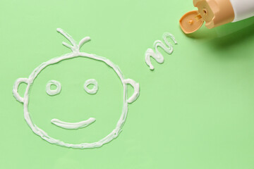 Drawing of baby face made with sunscreen cream on green background