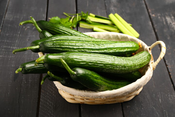 Wicker basket with fresh cucumbers on dark wooden background
