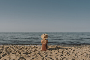 Aesthetic summer vacation fashion concept. Young tanned woman wearing a swimsuit and straw hat is...