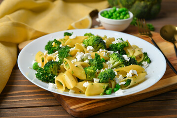 Plate with tasty penne pasta and broccoli on wooden background