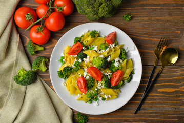 Plate with tasty penne pasta and vegetables on wooden background