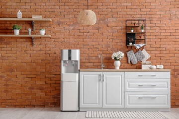 Interior of kitchen with modern water cooler near brick wall