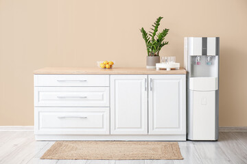 Interior of kitchen with modern water cooler near beige wall