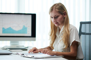 Smiling young businesswoman working with documents, checking data in marketing research