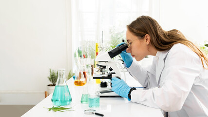 Young Caucasian woman scientist looking through a microscope in a laboratory for doing research. Students analyze biochemical by microscope research in the lab for discovering new medicine.