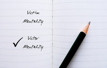 Notebook with pencil writing VICTIM and VICTOR MENTALITY, to overcome feeling like have no control...