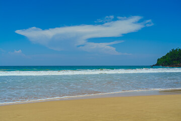 Sandy beach with low waves and clouds in the blue sky