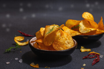 Bowls of homemade potato chips served with chili, parsley, seal salt on black stone background