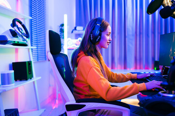 Young Caucasian woman professional gamer wearing yellow hoodie sits on a chair with a gaming table with pc, keyboard, monitor, microphone. Prepare for competition, cast gameplay or record a podcast. © artitwpd