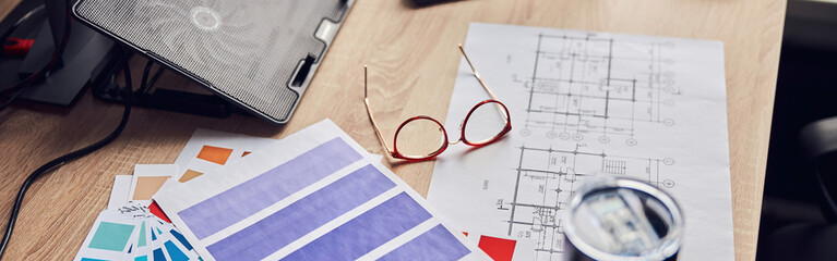 Close up shot of glasses, architectural blueprint with papers and color samples, thermos flask on...