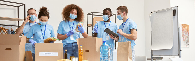 Full length shot of volunteers in protective masks and gloves sorting, packing food and water in...