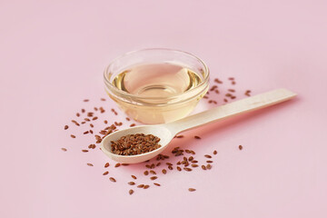 Bowl with flax oil and spoon of seeds on pink background