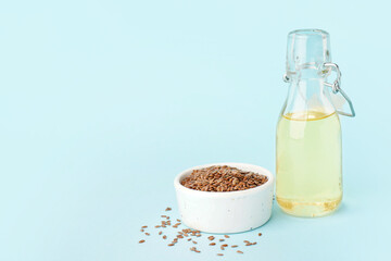 Bowl with flax seeds and bottle of oil on blue background