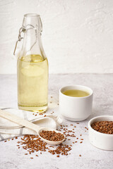 Bottle, glass with flax oil and seeds on light grunge background
