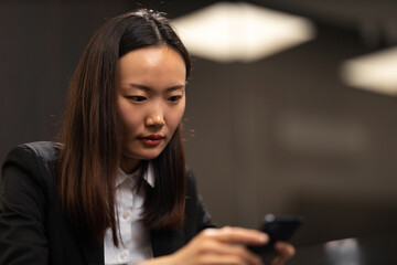 A shot of an elegant Chinese businesswoman using her smartphone in the conference room.