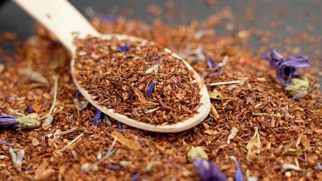 Rooibos flower herbal tea scattered on a wooden bamboo spoon close up. Rotation. Relax healthy drink