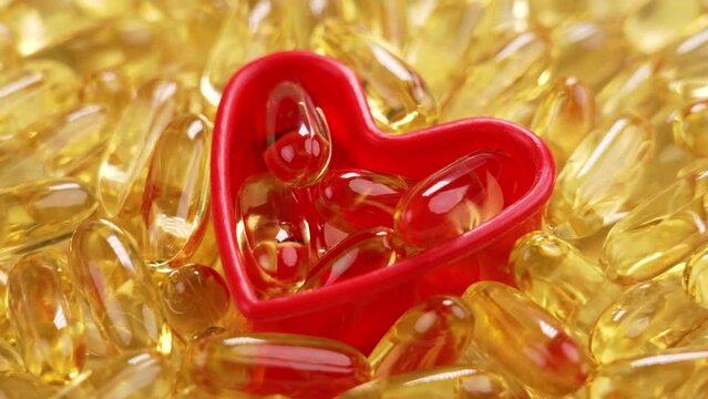 Golden Omega 3 supplement with sea fish oil. Natural yellow capsules in red heart shape. Close up