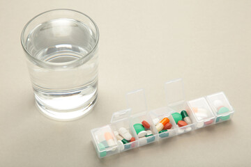 Pill box with medicaments and glass of water on grey background. Space for text