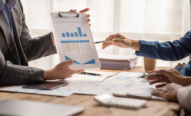 Group of confident business people point to graphs and charts to analyze market data, balance sheet, account, net profit to plan new sales strategies to increase production capacity.	