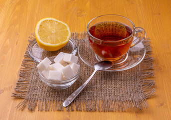 A teapot and a glass cup with brewing black tea. Next to the sliced lemon and lump sugar. Beautiful bright wooden background.
