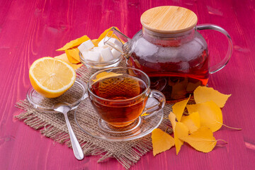 A teapot and a glass cup with brewing black tea. Next to the sliced lemon and lump sugar. Beautiful bright wooden background.