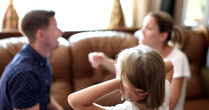 Little girl covers ears with hands against background of swearing parents at home. Soors and screams in family and the upbringing of children