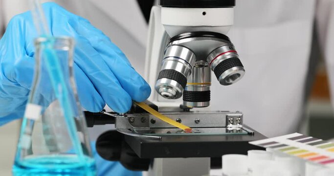 Scientist dips pH test strip into toxic liquid under microscope. Working with chemicals in chemistry lab