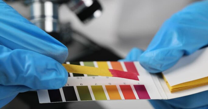 Hand is holding pH indicator and comparing color with scale. Check pH value in laboratory