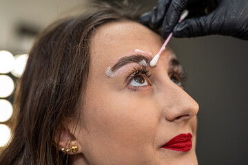 an eyebrow artist is laminating the eyebrows of a beautiful client.