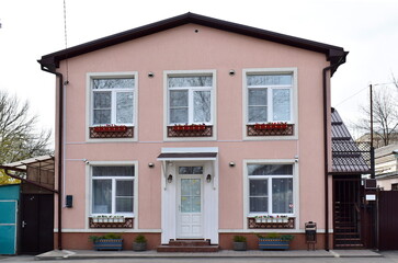 Fototapeta na wymiar residential pink house on two floors with flowers in pots under the windows