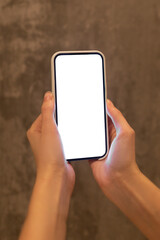 Young girl holding a phone with a white screen in a dark room. Mockup. Blank space for ad and logo. Vertical. Copy space.