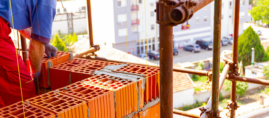 Worker is building wall with red blocks and mortar